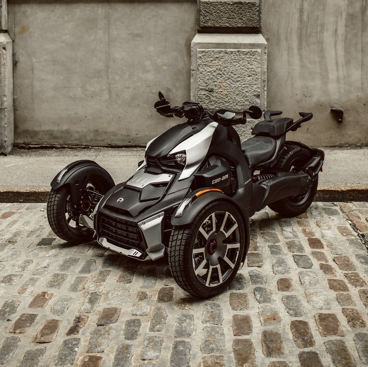 Can-Am Ryker three-wheeler with black passenger comfort seat installed, parked on cobblestone street