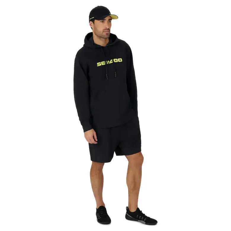 Man wearing a black Sea-Doo Men's Signature Pullover Hoodie with shorts and a cap, perfect for casual outdoor adventures.