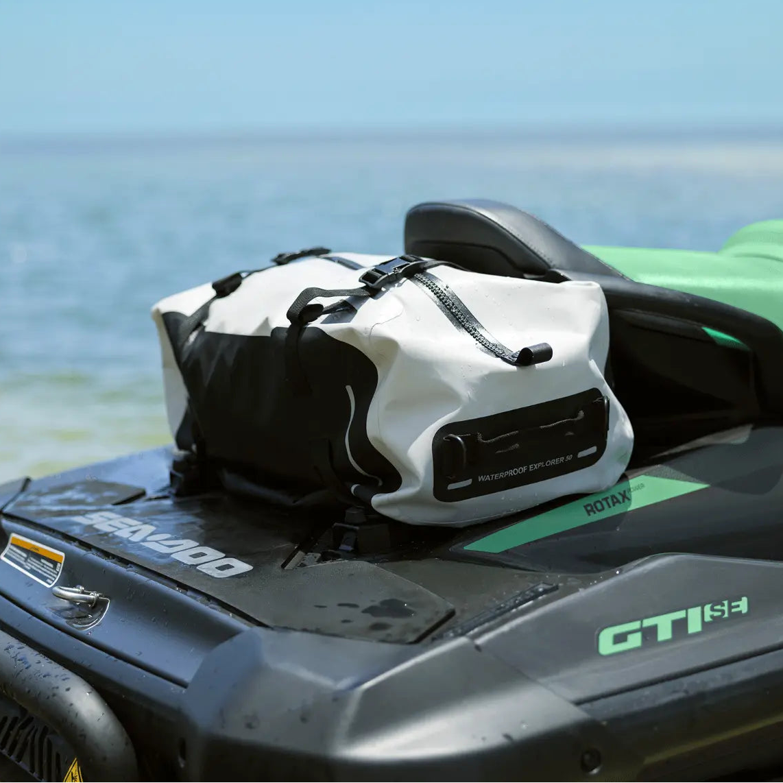 White waterproof bag on a green and black watercraft with ocean in the background