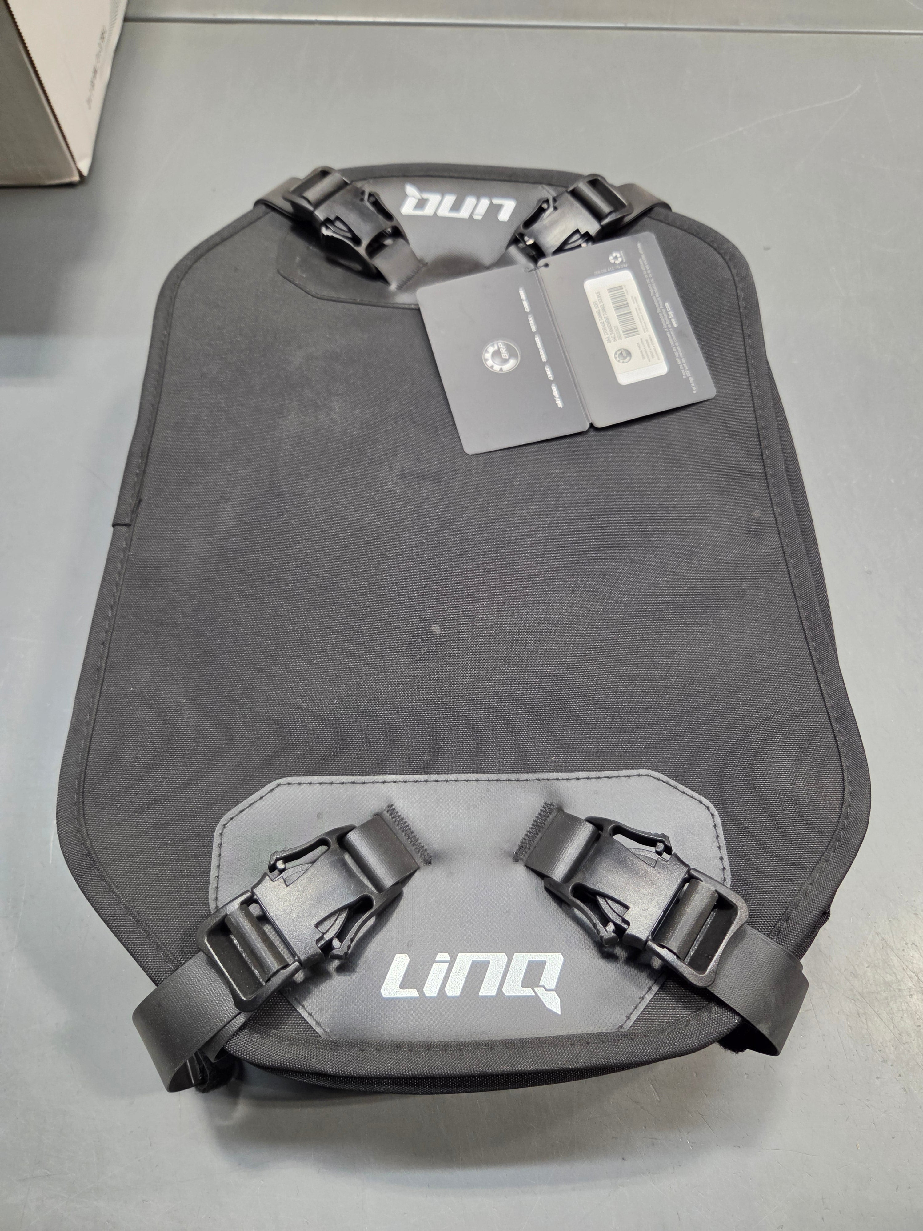 A dark gray protective motorcycle armor plate with adjustable black straps and white 'Lingo' branding, shown with its retail tag on a gray background.