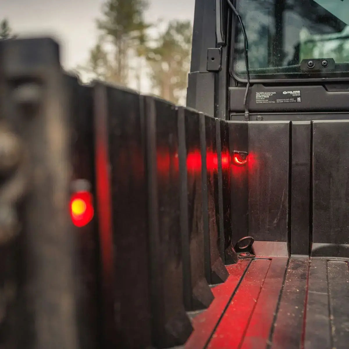 Close-up of a black truck bed with red lights on a blurred natural background