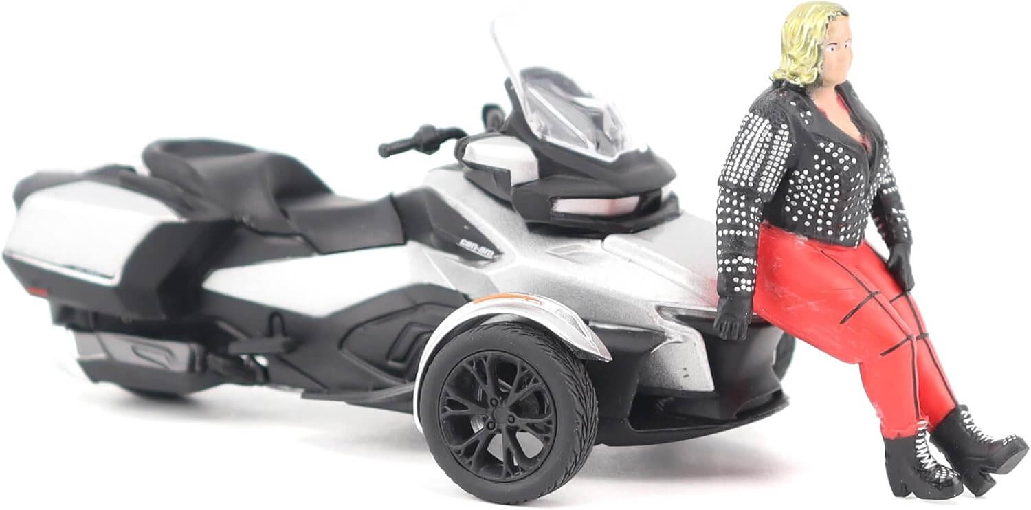 Model of a three-wheeled motorcycle with a person in a studded jacket and red pants sitting on it.