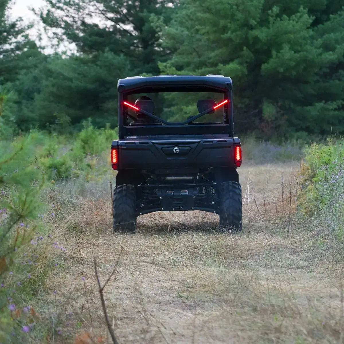 Black off-road vehicle driving through a forested area with red lights on.