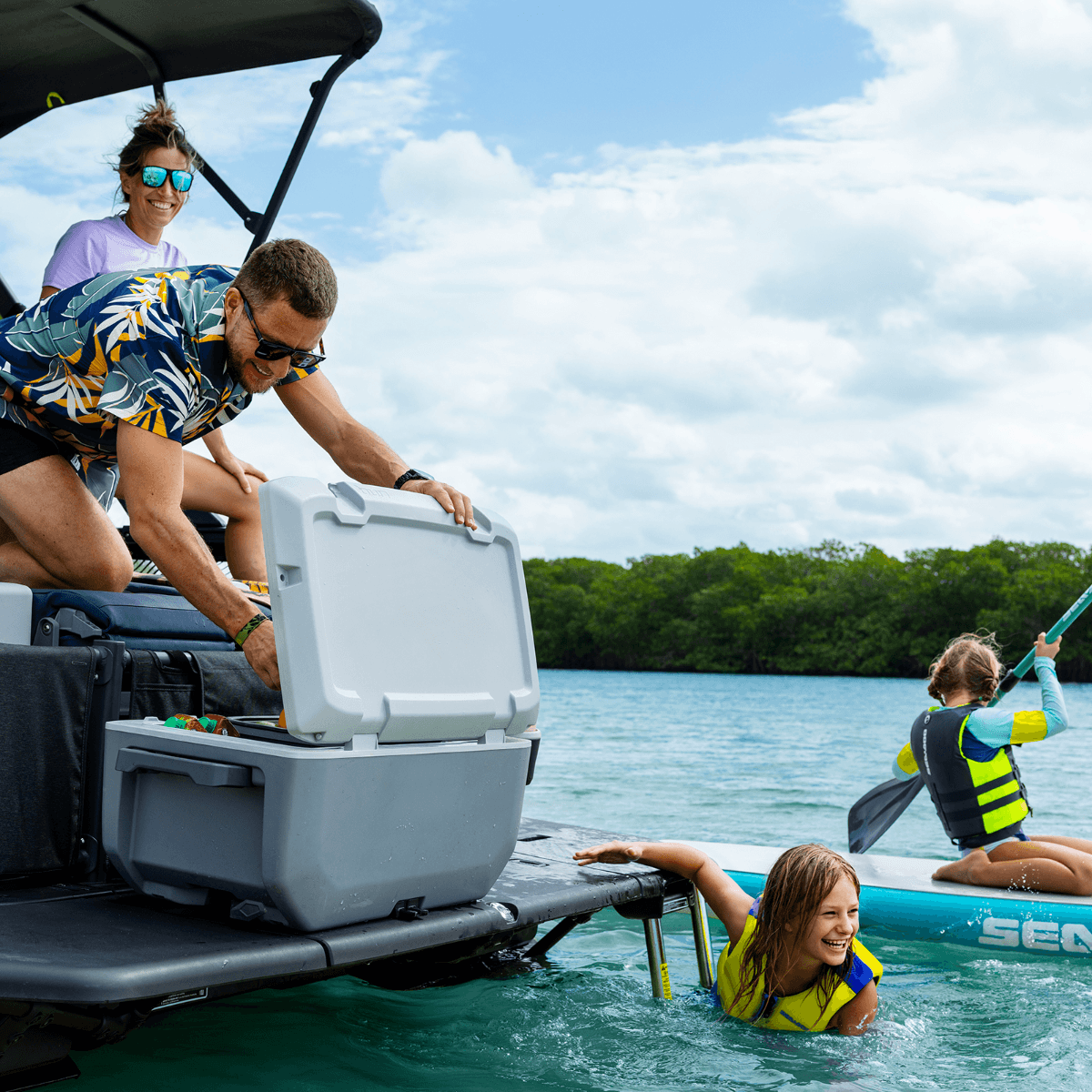 Family opening Sea-Doo cooler on Switch pontoon swim platform with kids swimming and paddleboarding nearby