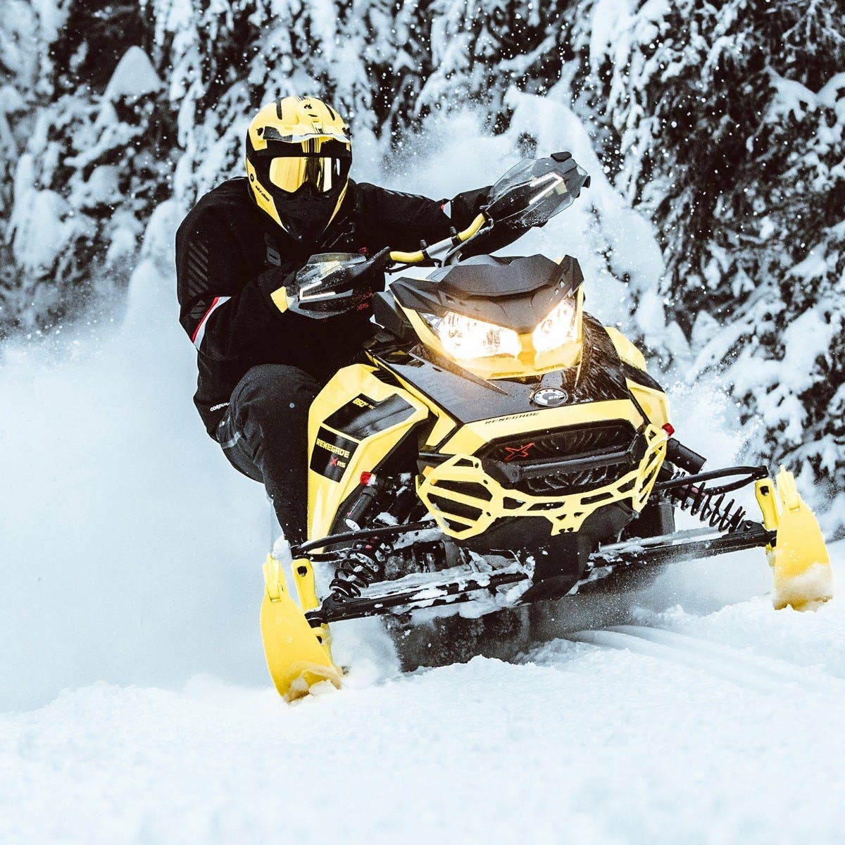 Rider on yellow Ski-Doo Renegade X-RS with Signature LED handguard lights lit up in snow