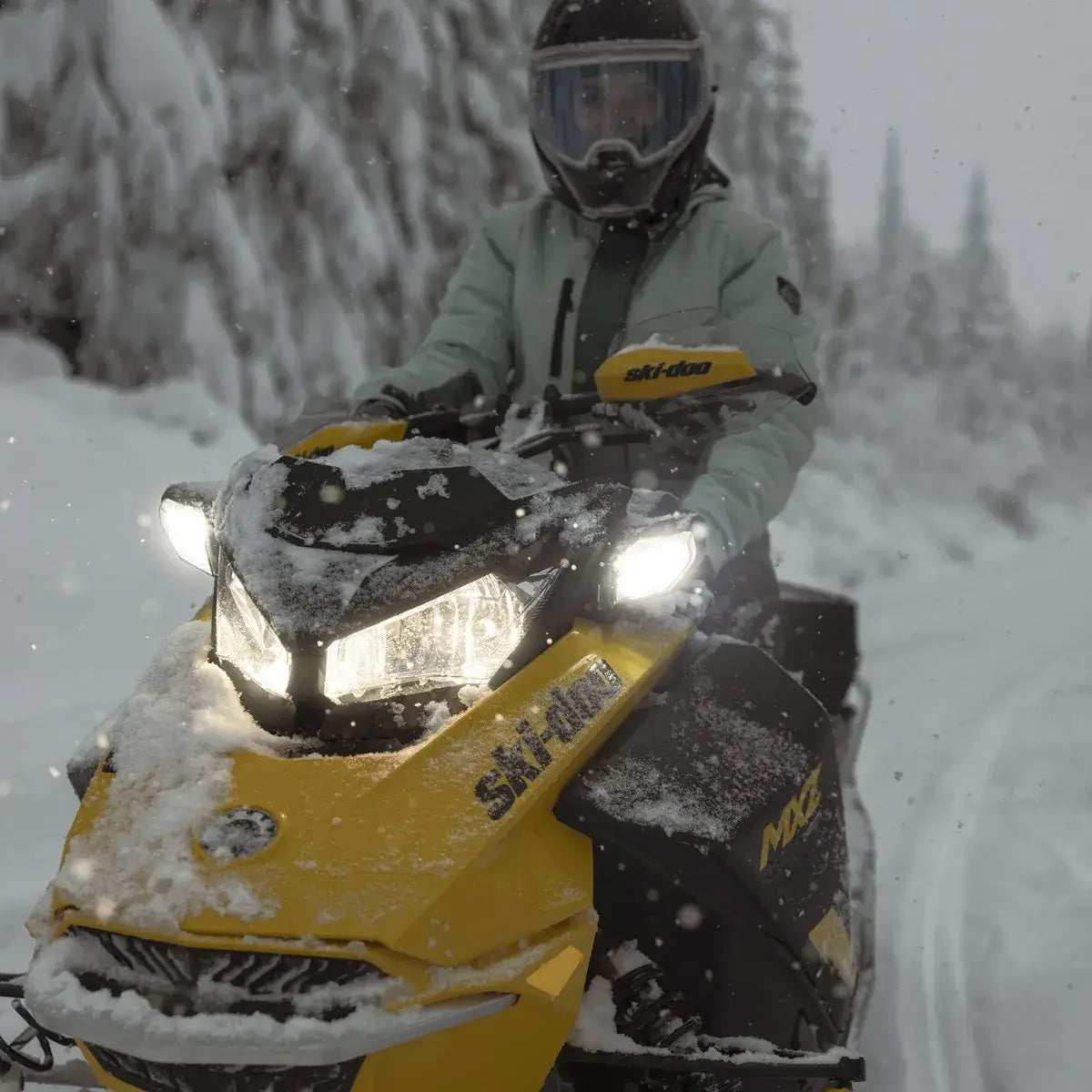 Person riding a yellow snowmobile in a snowy forest