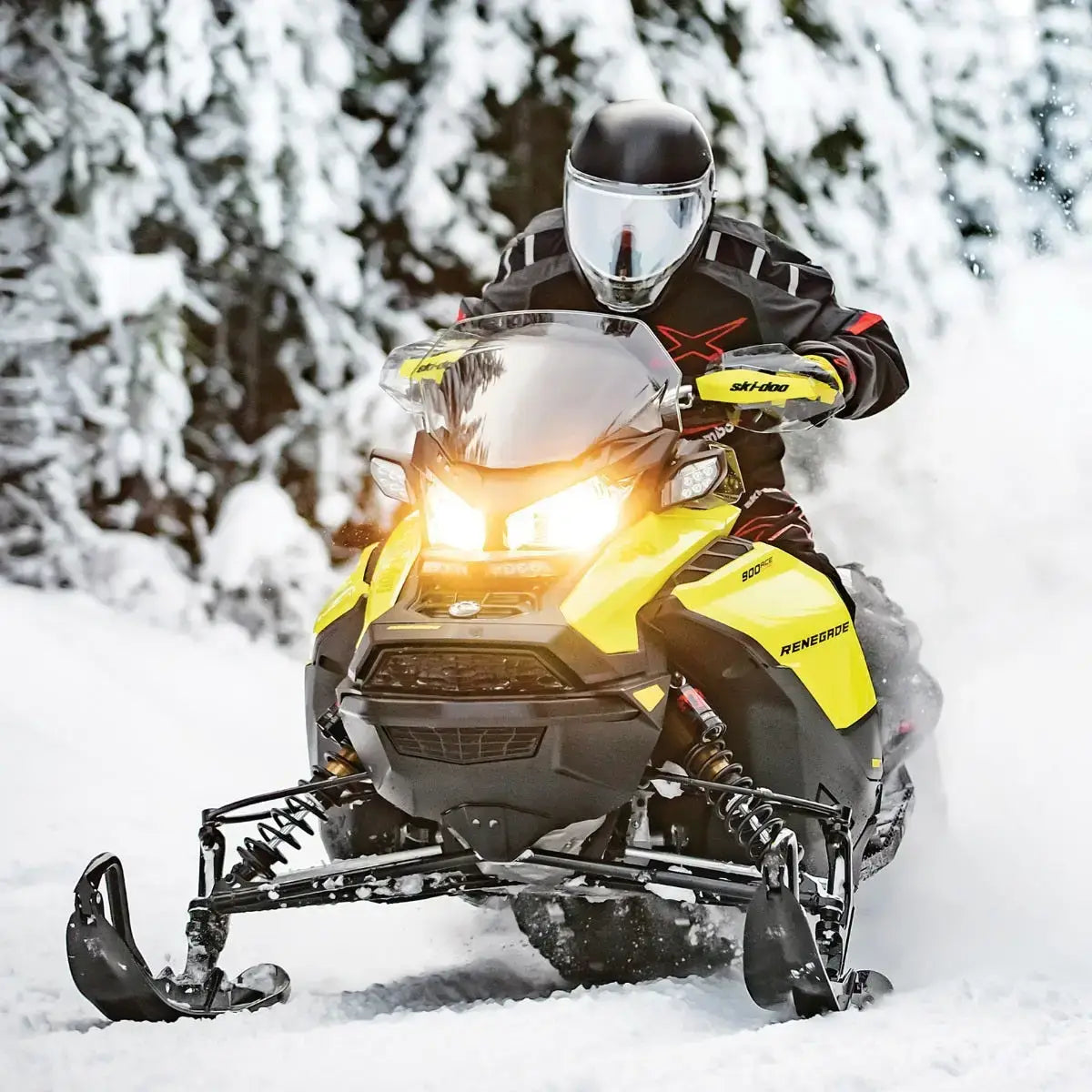 Person riding a yellow and black snowmobile in a snowy forest