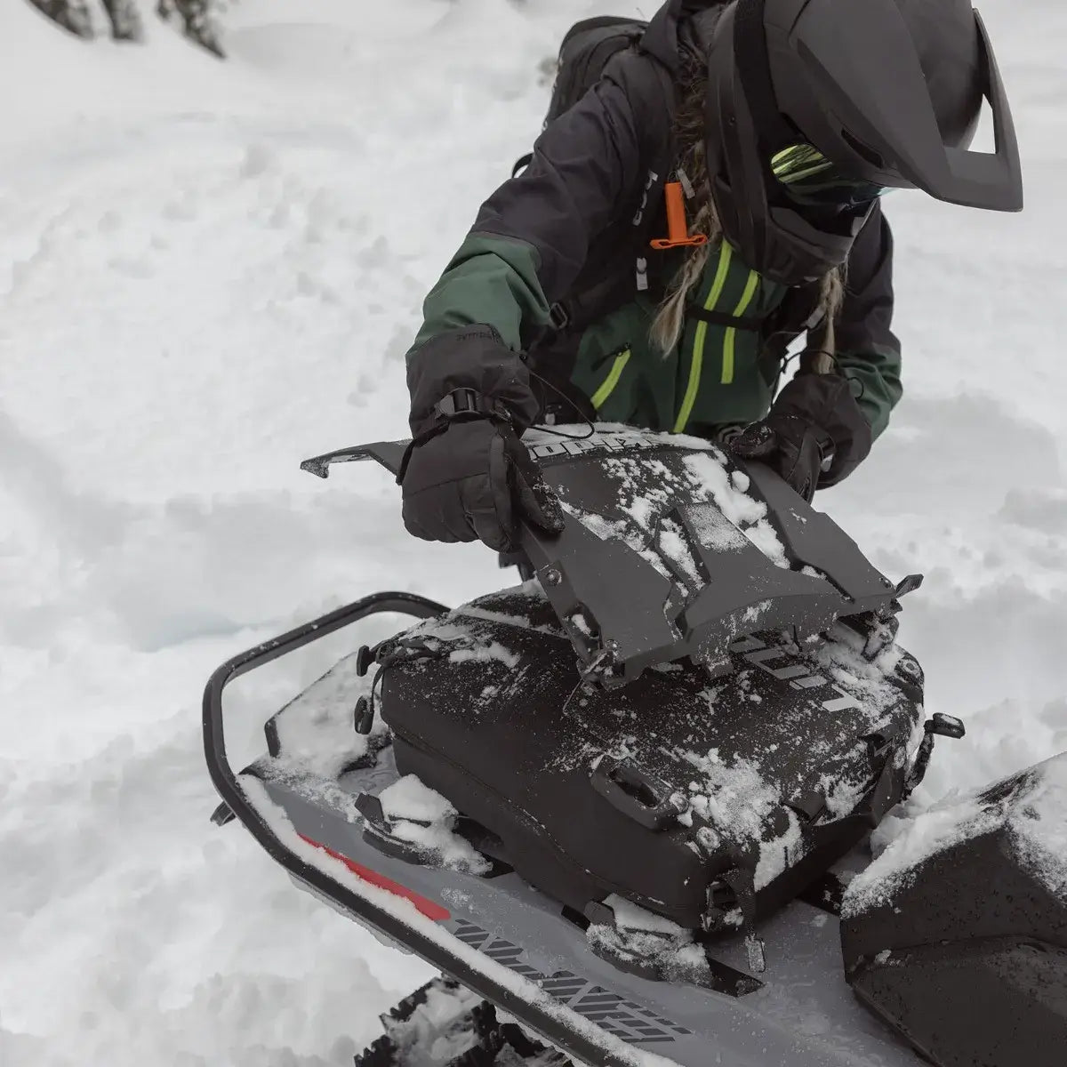 Person adjusting a snowmobile in a snowy landscape