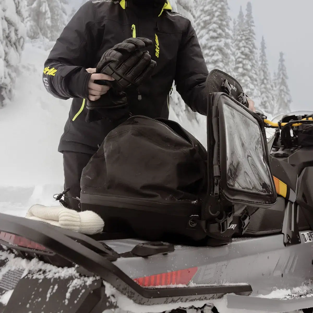 Person in winter gear with a storage bag on a snowmobile in a snowy landscape
