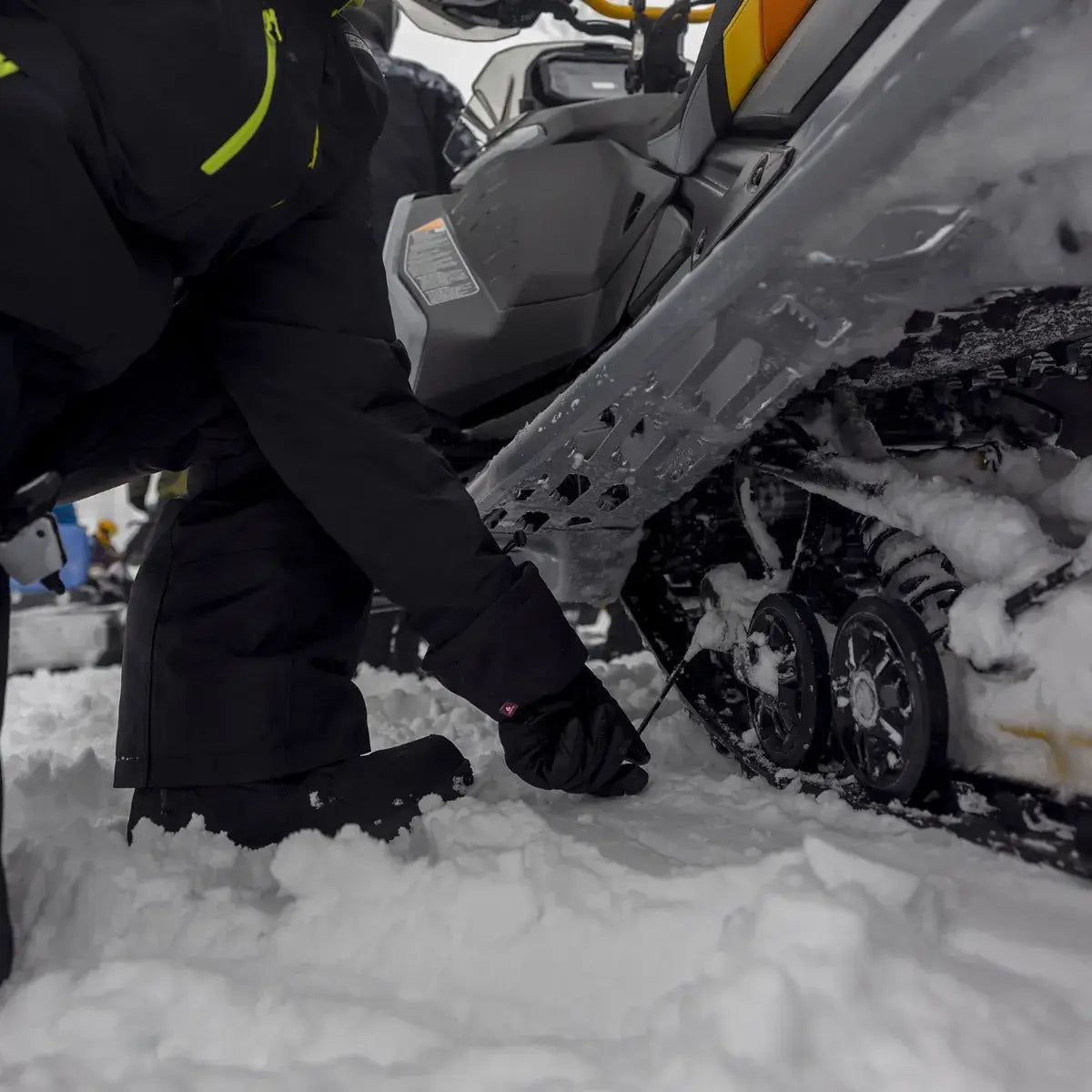 Person adjusting a snowmobile in a snowy environment