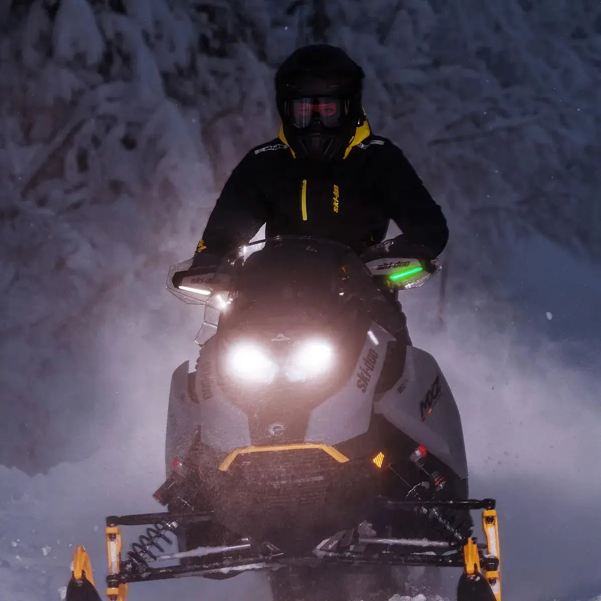 Person riding a snowmobile in a snowy forest at night