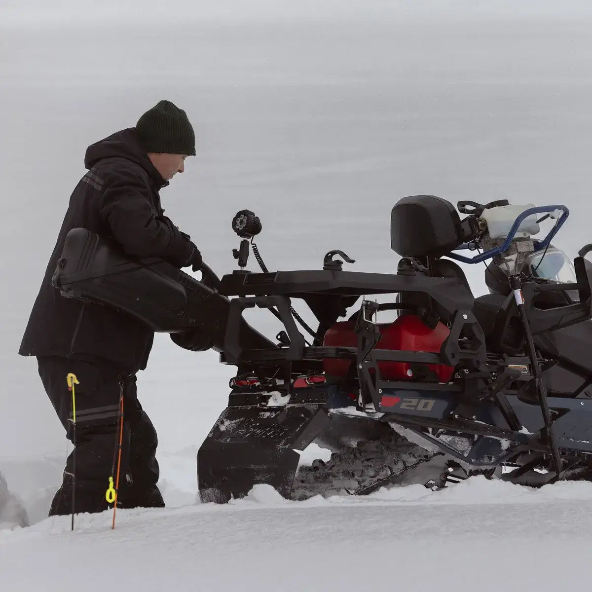 Person in winter clothing interacting with a snowmobile in a snowy landscape