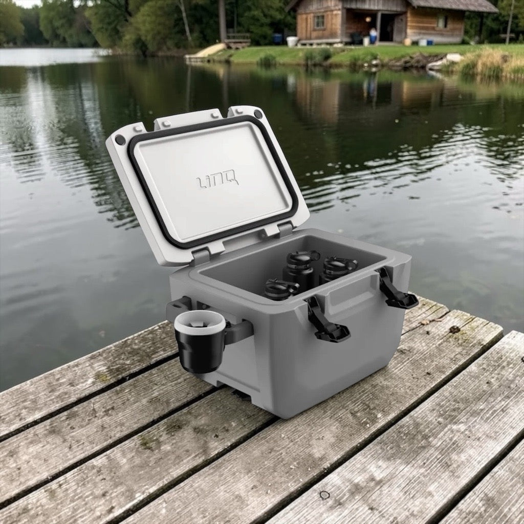 Gray cooler box with black handles and cup holder on a wooden dock by a lake.