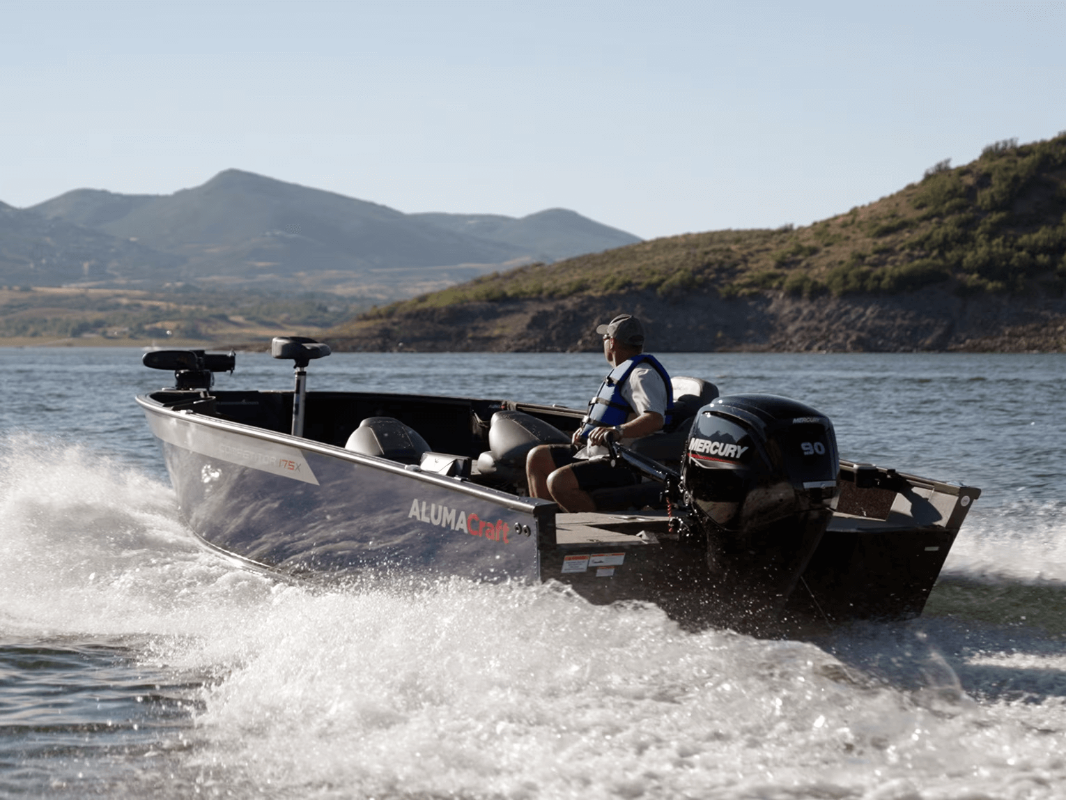 Person driving a boat on a lake with mountains in the background