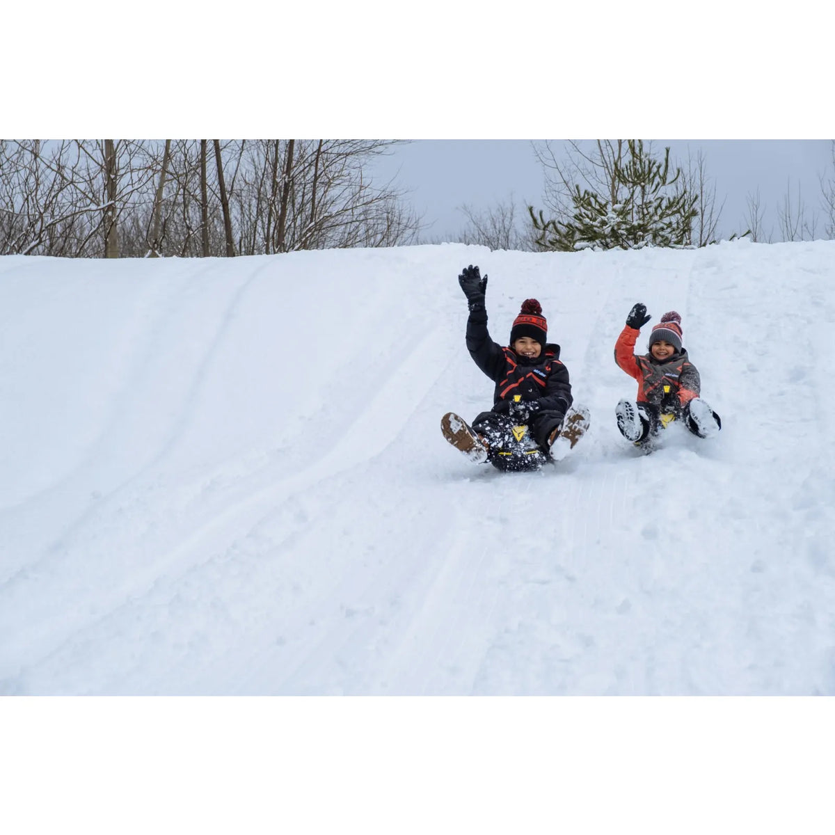 Two kids riding Ski-Doo Mini Snow Sleds feet-first down a snowy hill, B106800000