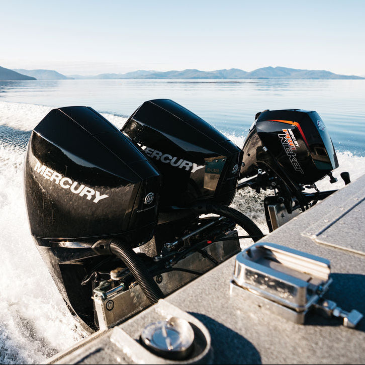 Boat with Mercury outboard motors speeding on water with mountains in the background