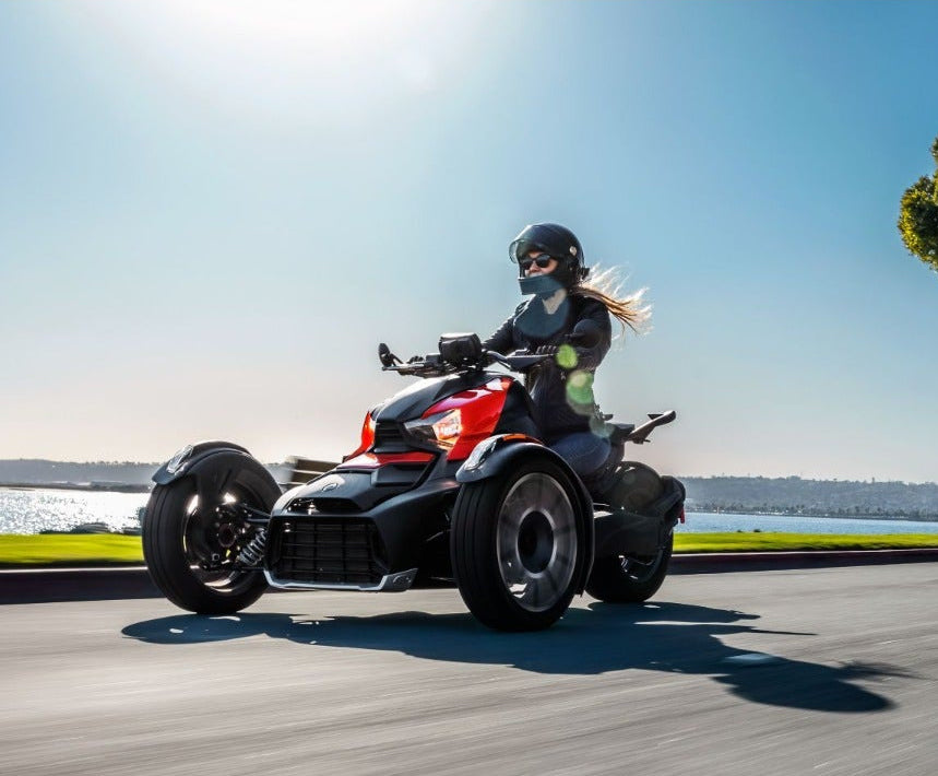 Rider on red Can-Am Ryker three-wheeler with classic side panels cruising coastal road
