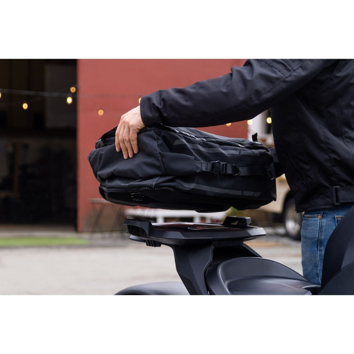 Rider mounting black LinQ 40L Urban Bag onto Can-Am motorcycle LinQ rack