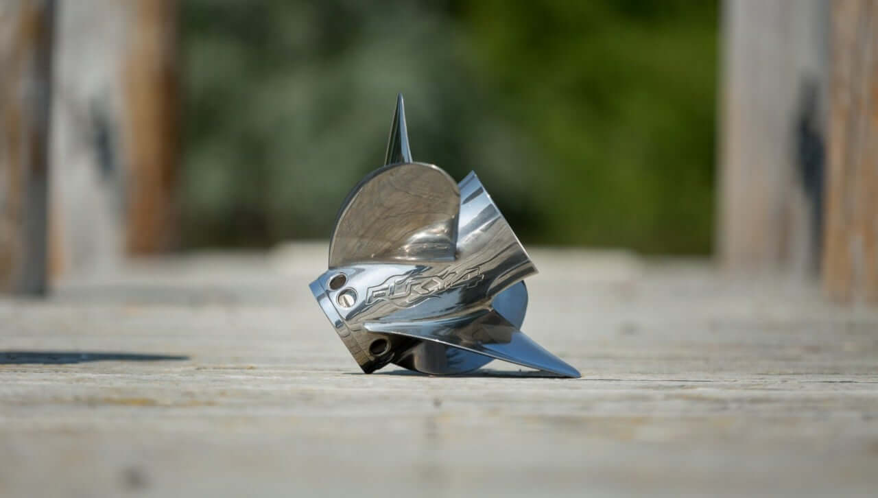 Metallic Mercury Marine propeller on a wooden surface with blurred natural background