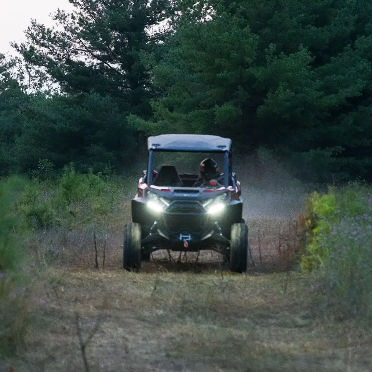can-am UTV driving through a forested area with headlights on