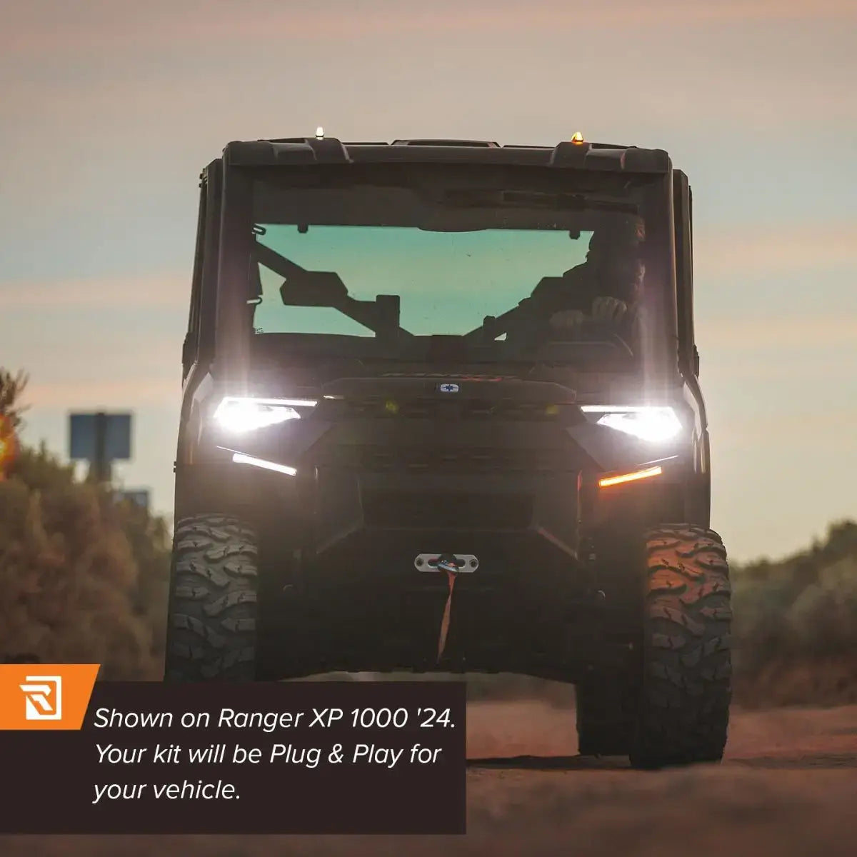 Front view of a vehicle with headlights on, driving on a road at sunset.