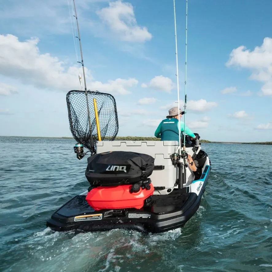 Person fishing on a small boat with a cooler and fishing equipment in the water.