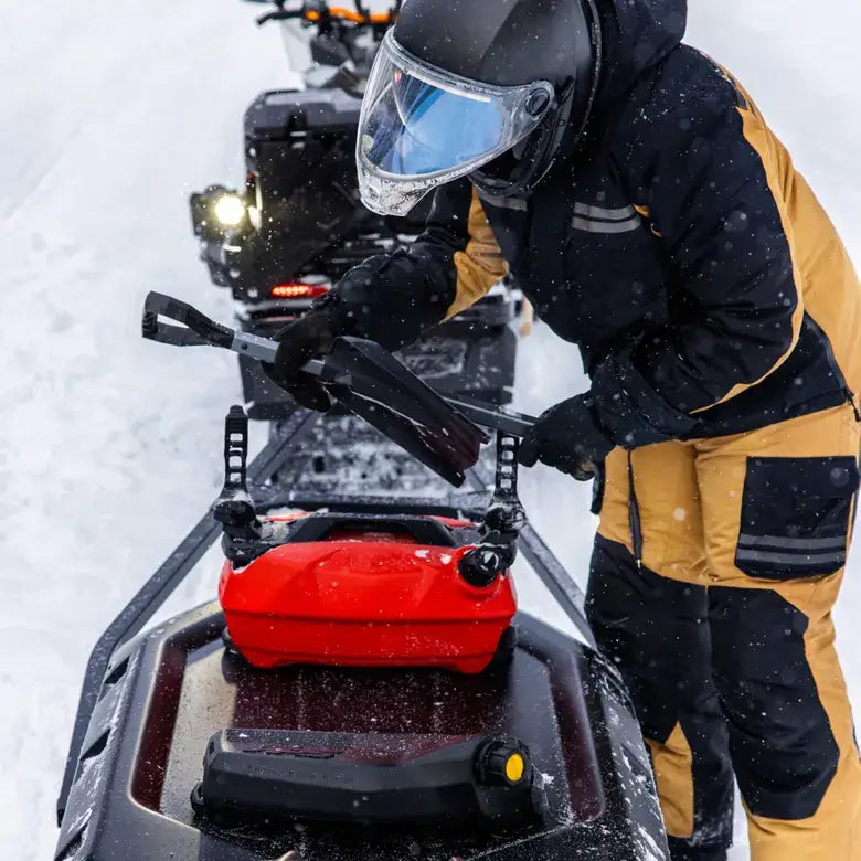 Person in winter gear preparing a snowmobile in a snowy landscape