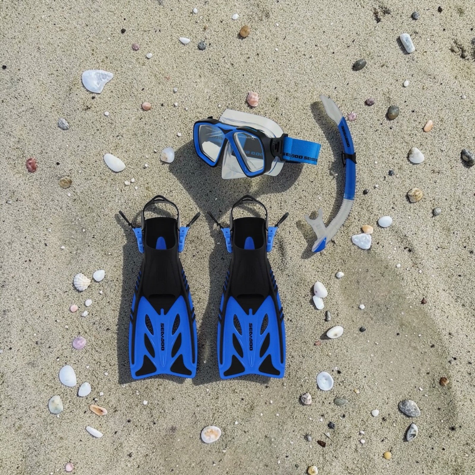 Blue snorkeling gear including mask, snorkel, and fins on sandy ground with shells.