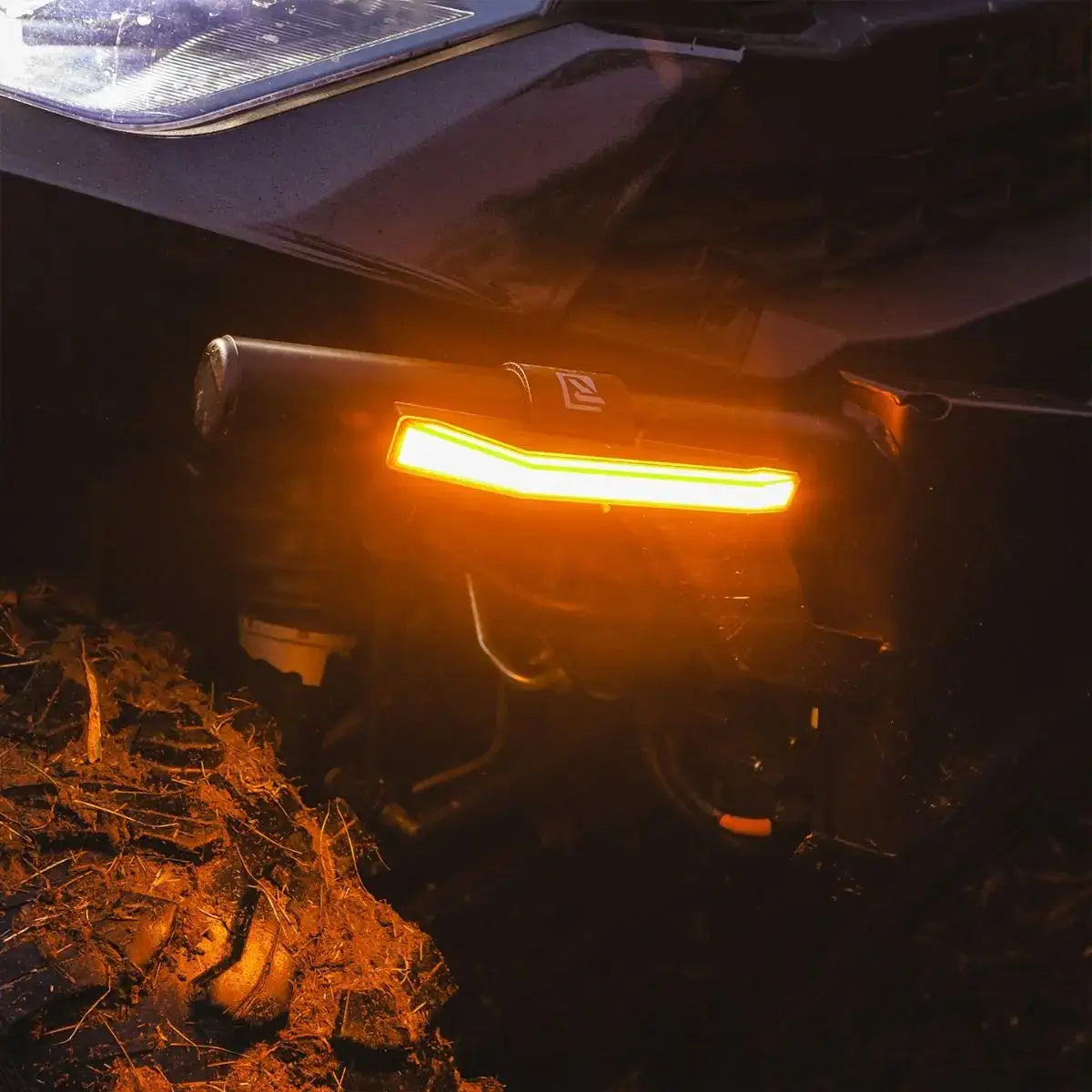 Close-up of a vehicle's headlight and front bumper in a dark forest setting.