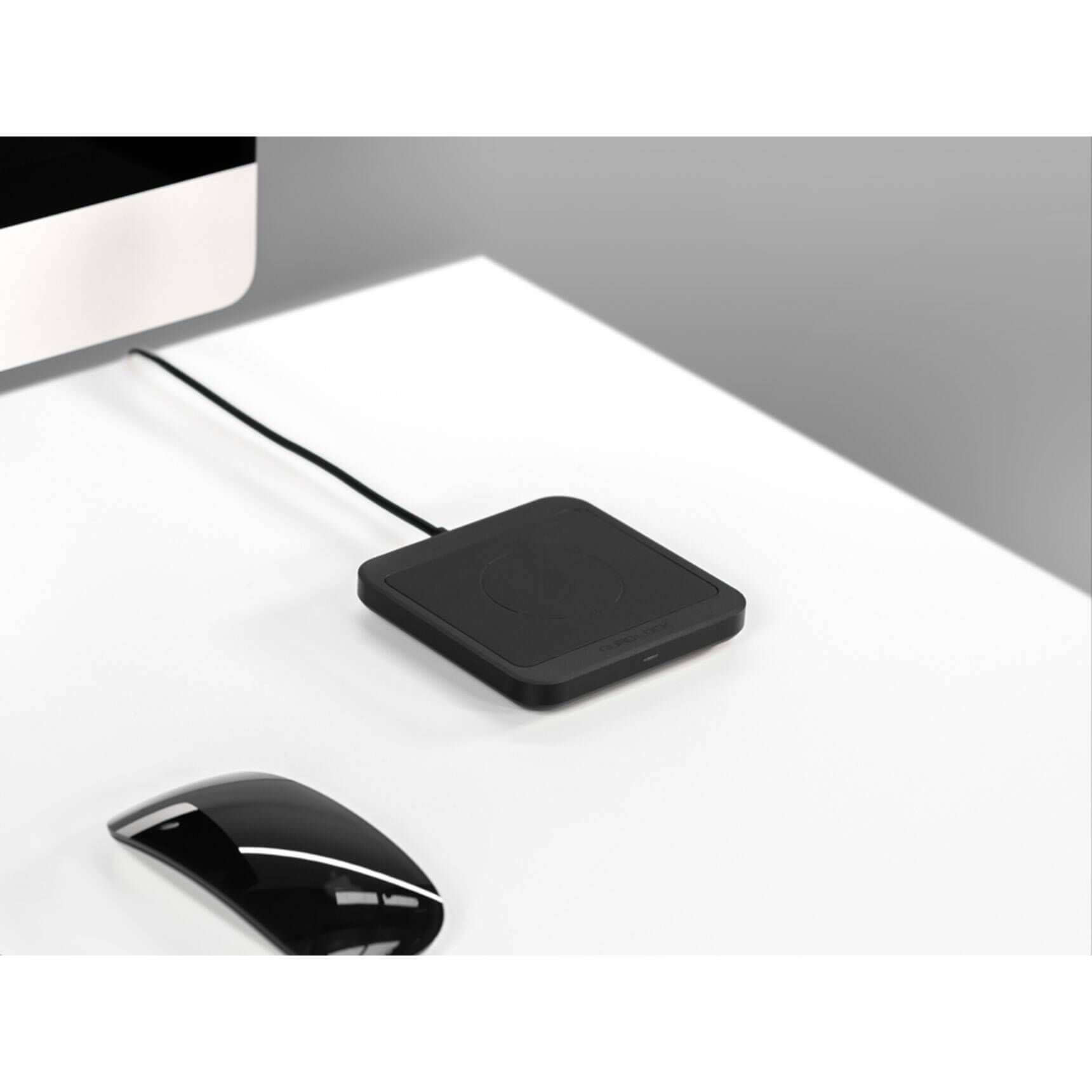 Black wireless charging pad on a white surface with a computer mouse nearby.