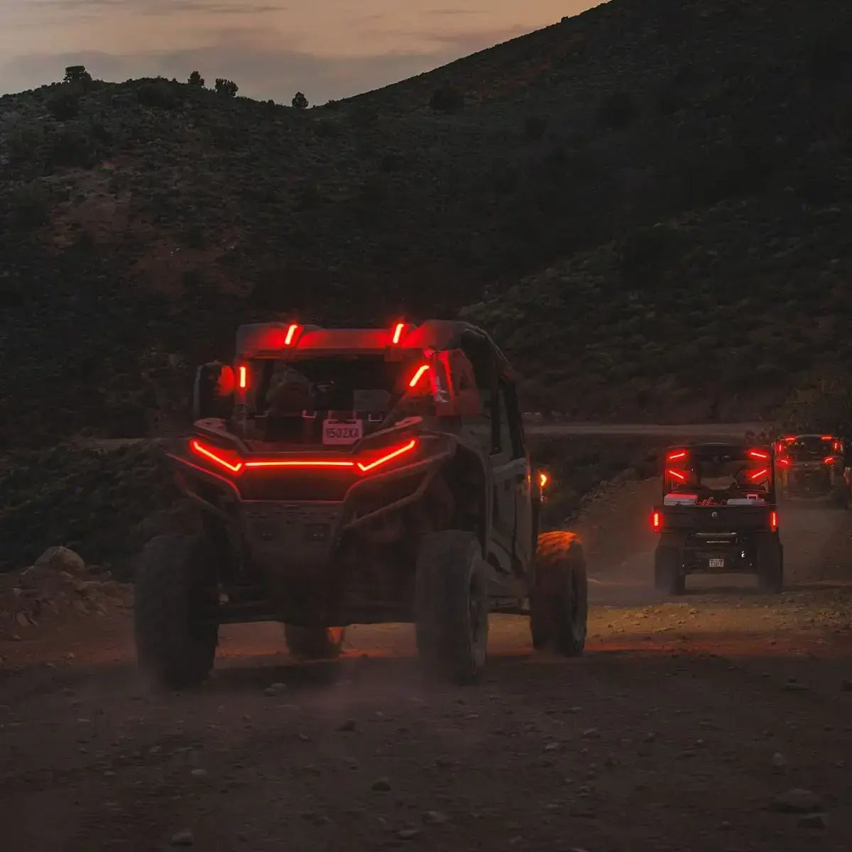 Two off-road vehicles on a dirt road at dusk with red lights illuminating the scene.