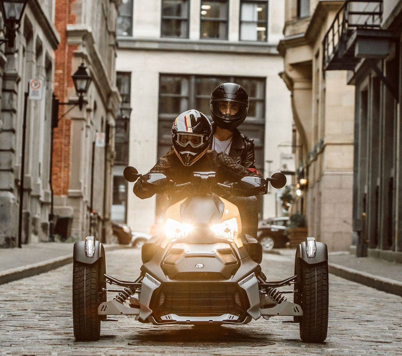 Can-Am Ryker three-wheeler with aluminum radiator protector, front view riders on cobblestone street