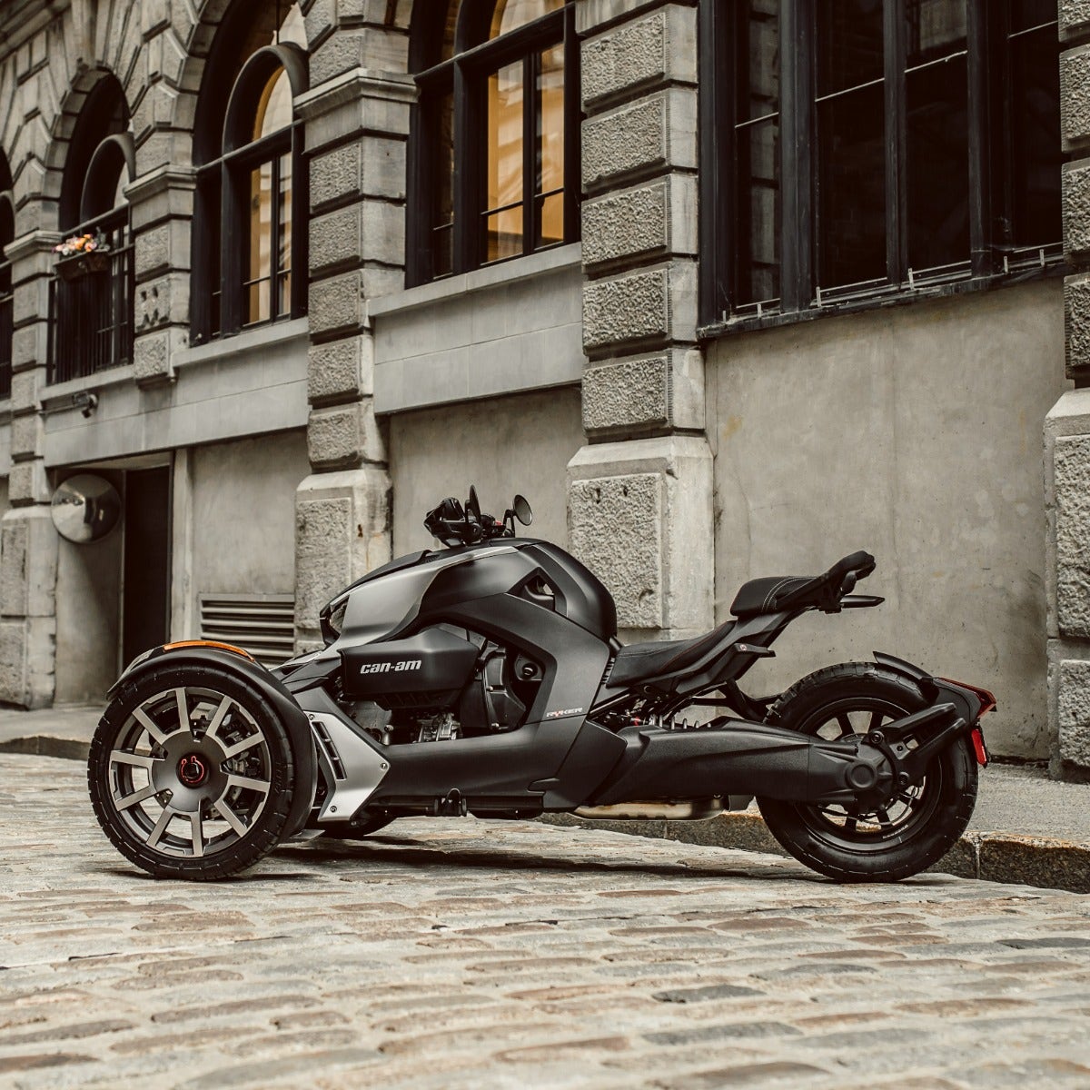 Can-Am Ryker three-wheeler with black comfort seat parked on cobblestone street, side view