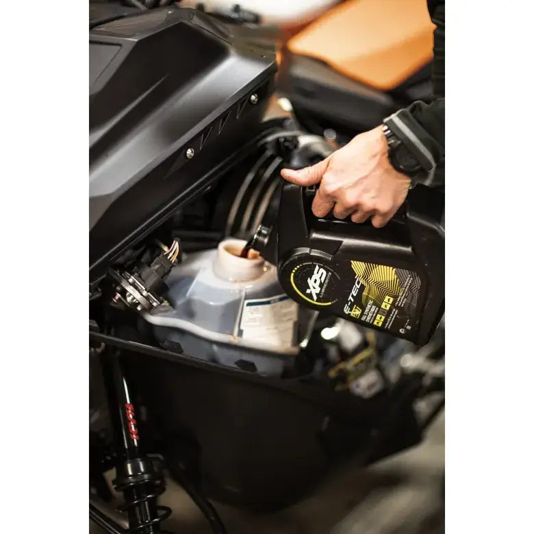 Person refilling a motorcycle's oil tank with a black oil can labeled 'YXZ'.