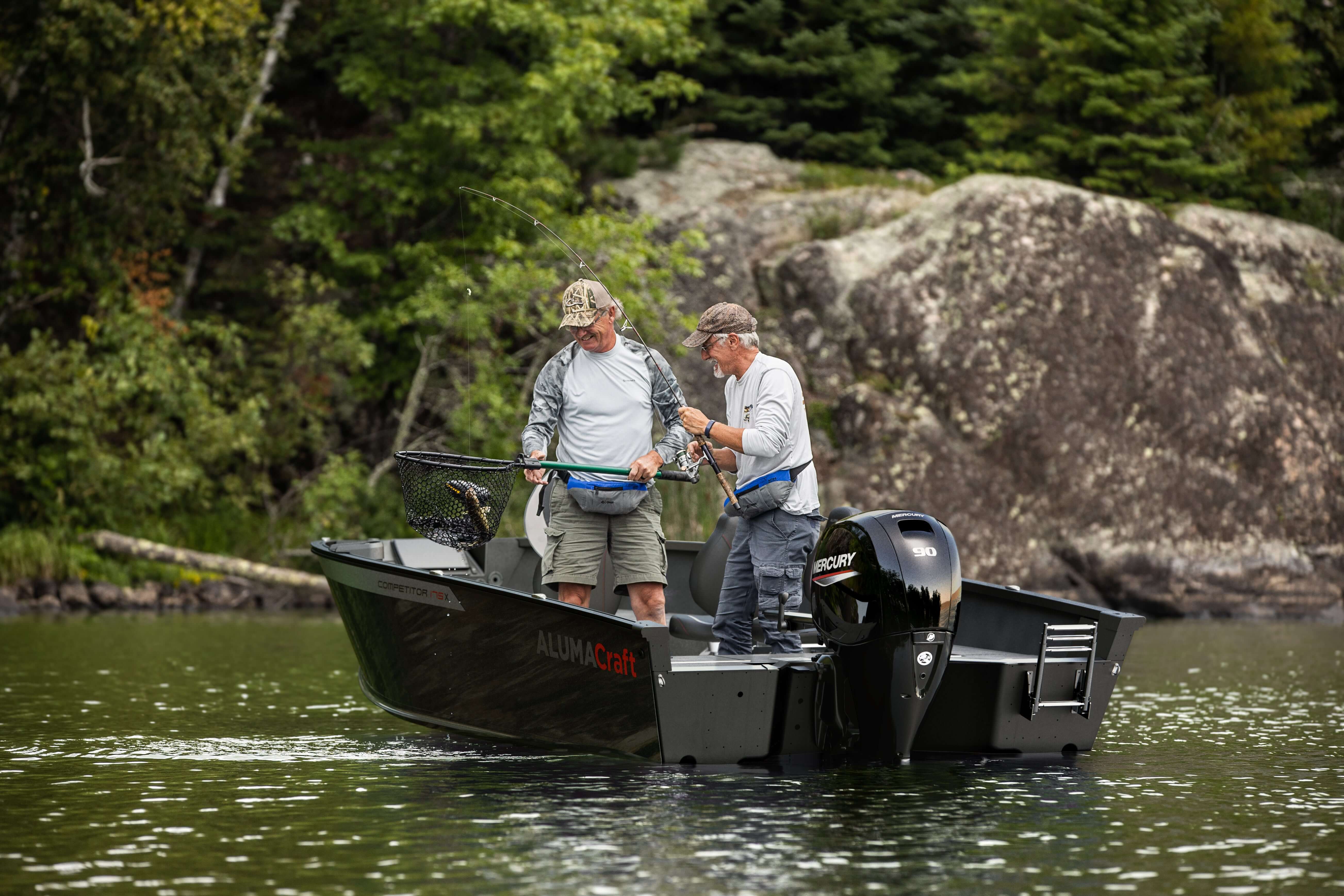 Two men on a boat in a lake with trees and rocks in the background
