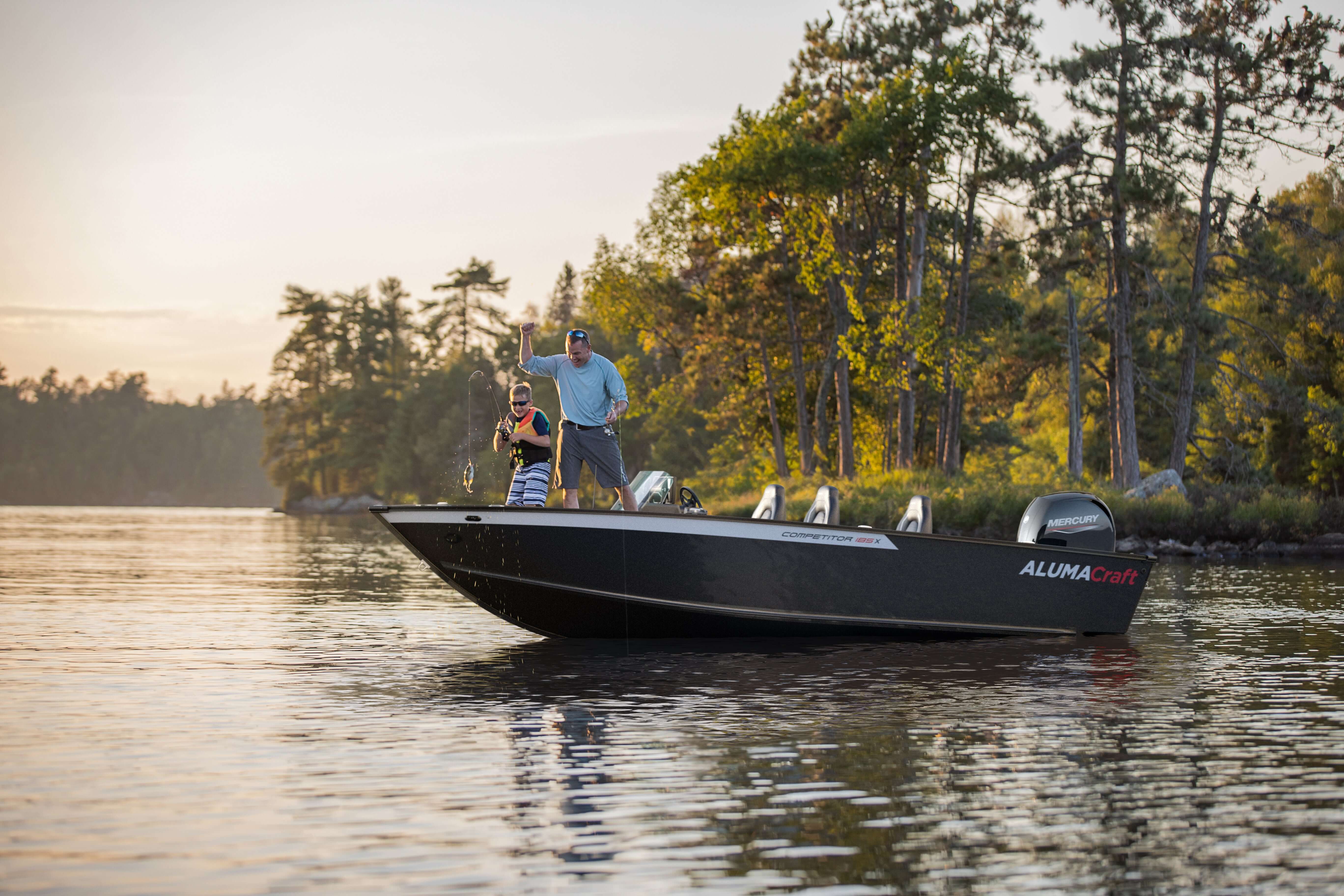 Man standing on a black Aluma boat on a lake with trees in the background