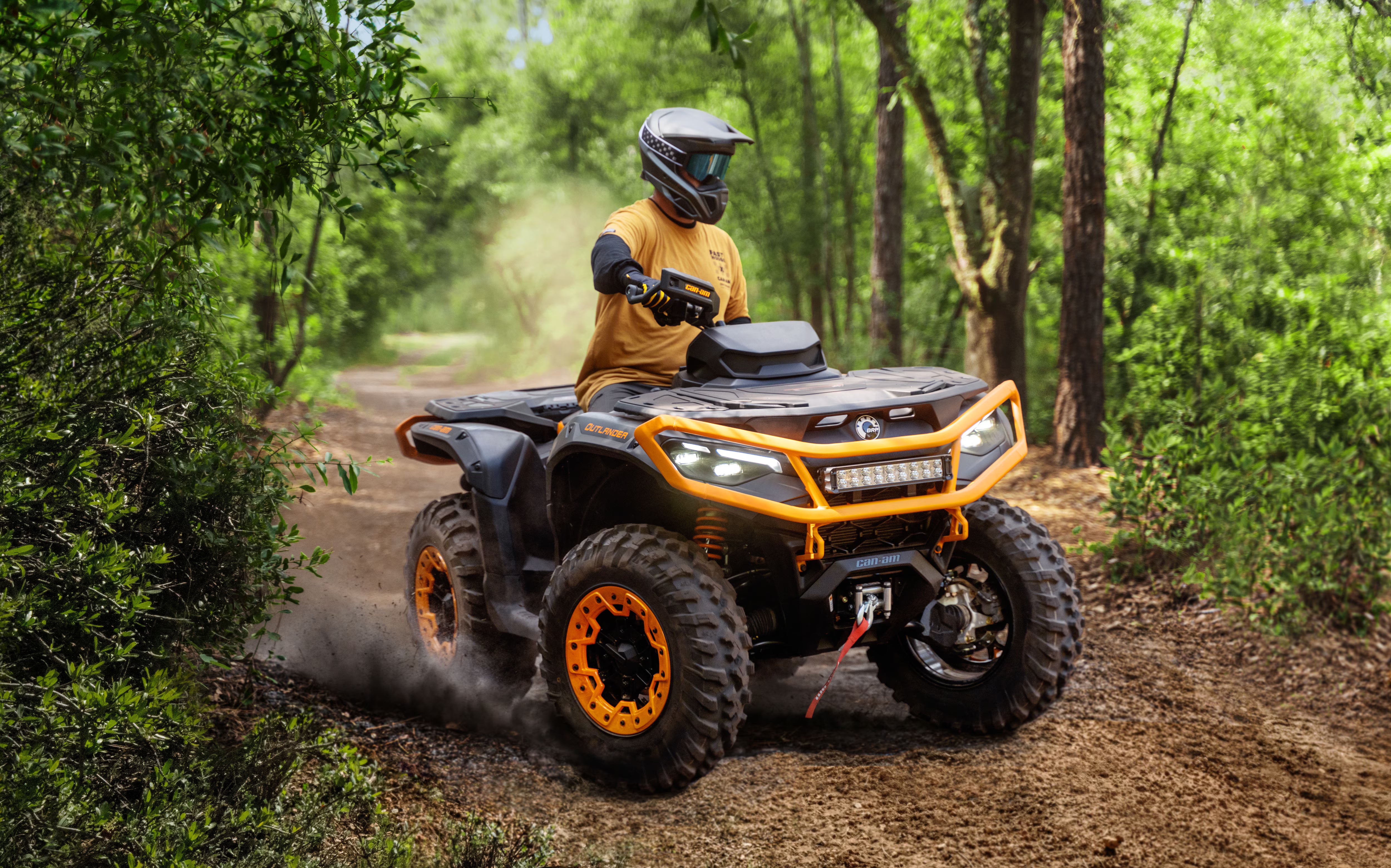 Person riding an orange and black Can-Am ATV through a forest