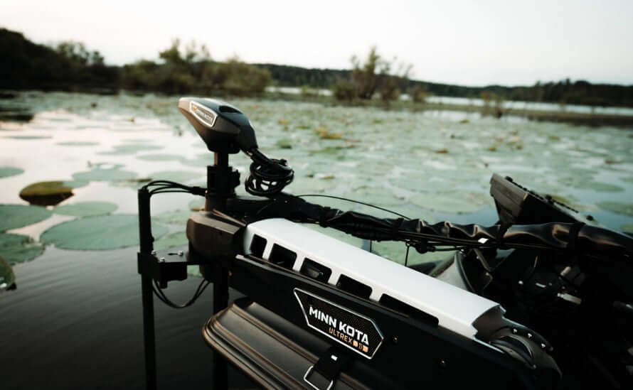 Minn Kota trolling motor on a boat with a lake and trees in the background
