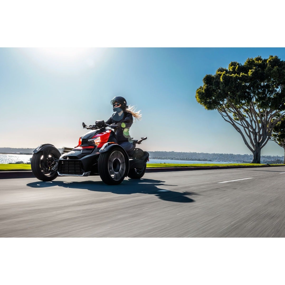 Rider on red Can-Am Ryker three-wheeler with classic side panels cruising coastal road
