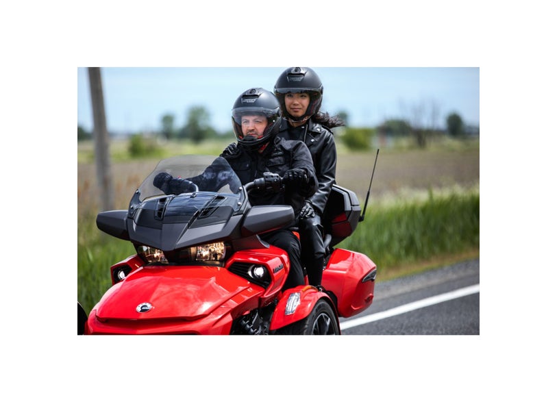 Red Can-Am Spyder F3 three-wheeler with auxiliary lights, two riders on roadway