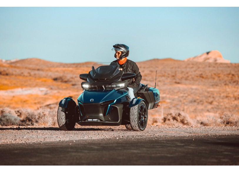 Can-Am Spyder RT three-wheeler with LED auxiliary lights parked on desert road, rider in helmet