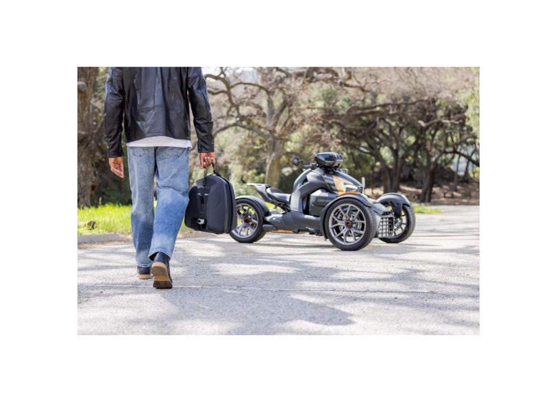 Rider carrying Can-Am Ryker LinQ 16L top case beside parked Ryker three-wheeler