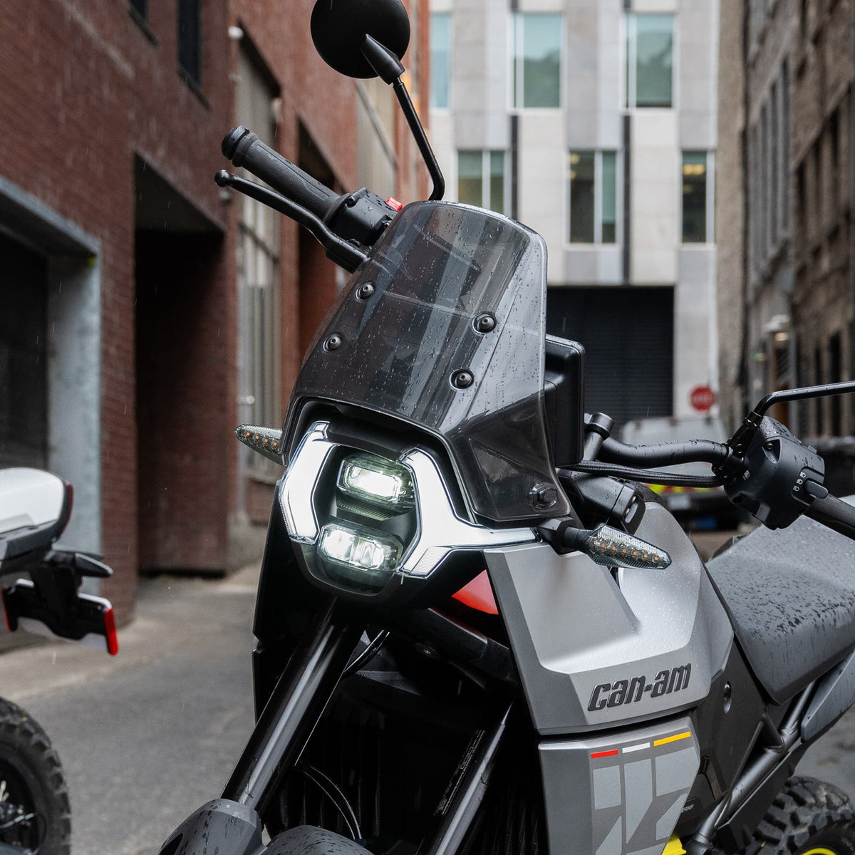 Can-Am Origin electric motorcycle front LED headlight and windscreen close-up in rainy alley