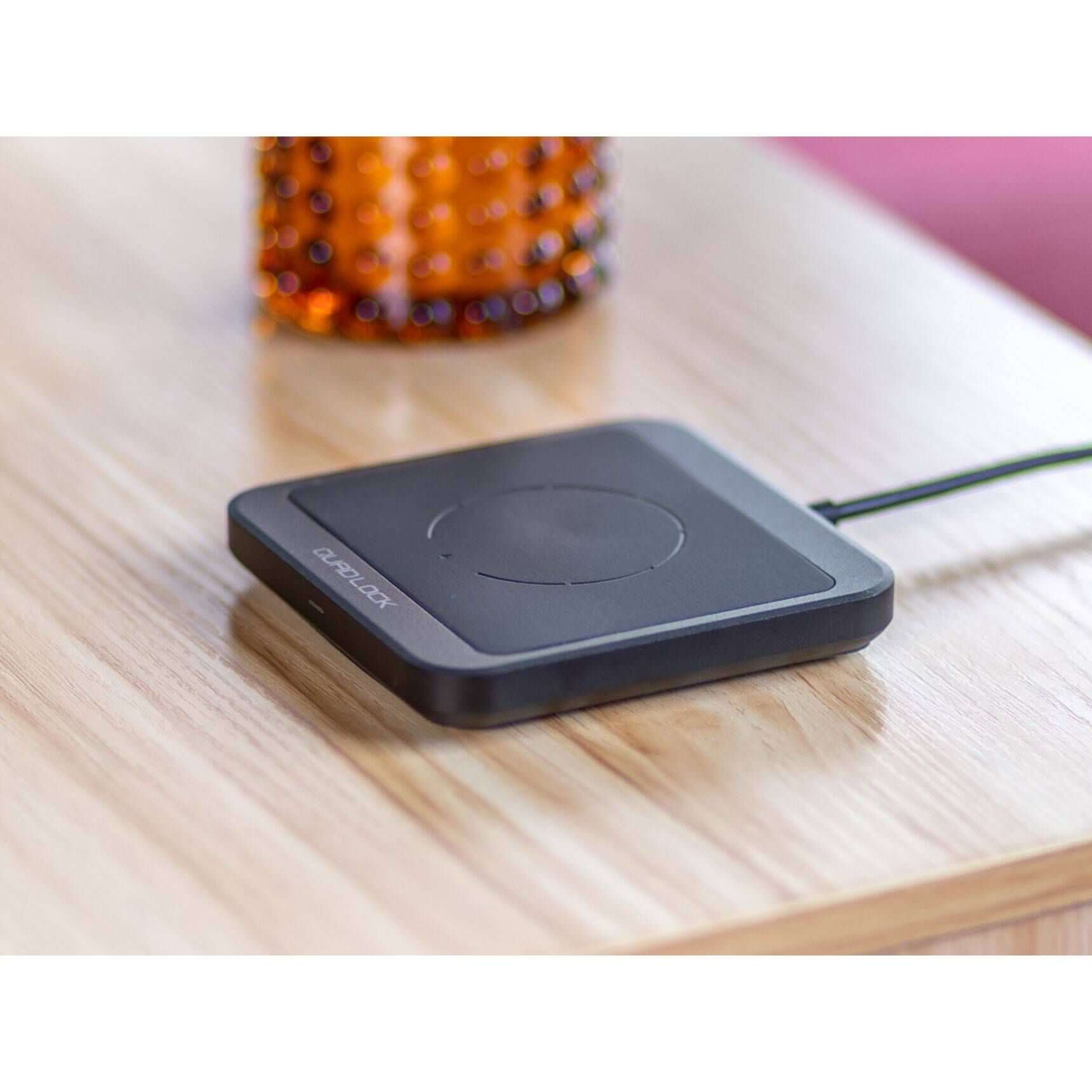 Black wireless charging pad on a wooden surface with a blurred colorful object in the background